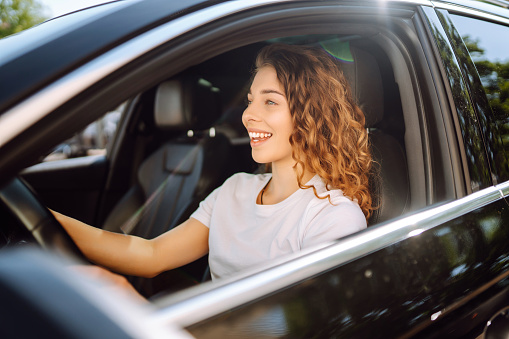 Female driver. Portrait of young woman is driving a car and smiling. Automobile travel.