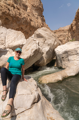 Mature women sitting on the rock at the rapids flowing among large rocks in oasis Wadi Bani Khalid.  Oman