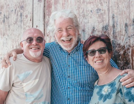 Happy group of senior friends or family hug standing against a wooden door expressing affection and care, elderly mature caucasian men and woman looking at camera smiling
