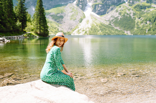 Portrait of a young woman in dress enjoys on a mountains along a lake. Adventure, travel, fashion, active life.