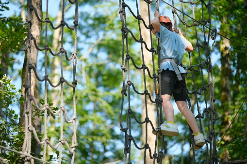Child having fun at outdoor extreme adventure rope park. Active childhood, healthy lifestyle, playing outdoors, children in nature.