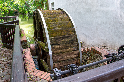 Wusterhausen, Brandenburg - Germany - 06-28-2022: An old mill wheel that no longer works on a house wall and a river made of wood and a mechanism to regulate the flow of water, called weir.