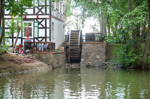 Wusterhausen, Brandenburg - Germany - 06-28-2022: A mill wheel at the end of a river on a house made of wood. The river has green water and the house is a half-timbered house.