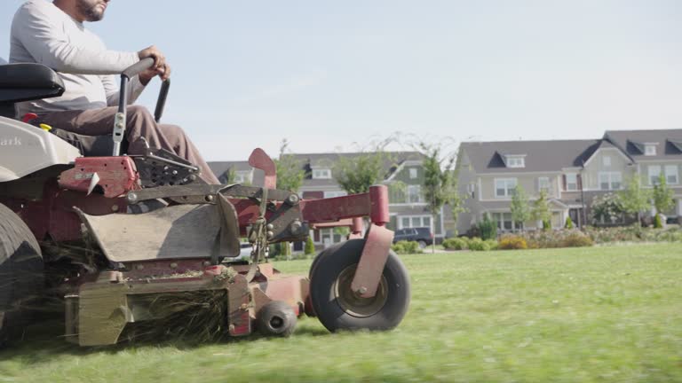 Low Angle View of a Latino Man Using a Riding Lawnmower near an Apartment Complex
