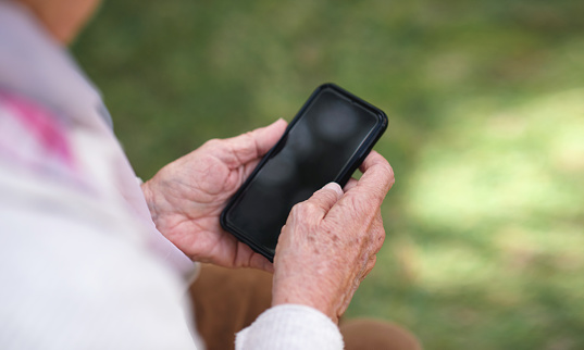 Old woman hands using smartphone texting sending messages on mobile phone outdoors