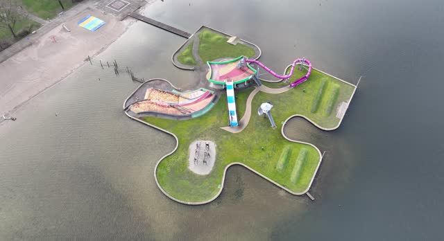 The water play island in the shape of a puzzle piece provides lots of water fun for young and old. Recreational playground swimming water surround it. Birds eye aerial drone view.