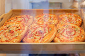 Small pizza with cheese, ham, tomatoes, pickles and sauce on a wooden tray on the store counter through the window