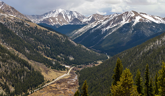 A panoramic overview of Highway 82 winding in Lake Creek Valley, with snow-capped La Plata Peak (center-left, 14,336 ft) of the Sawatch Range towering in background, on a stormy Spring day, as seen from the summit of Independence Pass (12,095 ft). Colorado, USA.