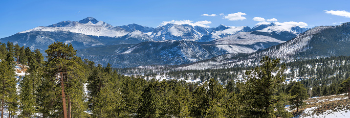 A panoramic view of snow-capped northern Front Range mountains, leading by majestic Longs Peak at left, on a sunny Spring day. Rocky Mountain National Park, Colorado, USA.