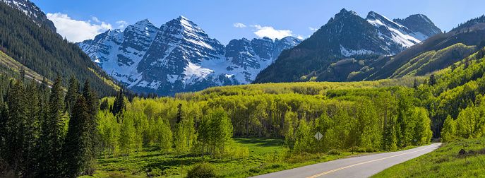 A panoramic view of Maroon Bells rising high in lush green Maroon Creek Valley, as seen from side of Maroon Creek Road, on a sunny Spring evening. Aspen, Colorado, USA.