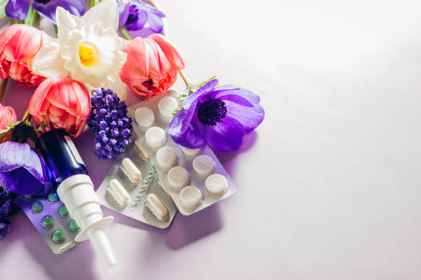 Seasonal spring allergy. Antihistamine pills and nasal spray flat lay with purple pink flowers. Healthcare for allergic.