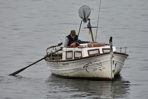 Vigo, Pontevedra, Spain; March,04,2021; a small fishing boat with an old fisherman prepares the gear for fishing