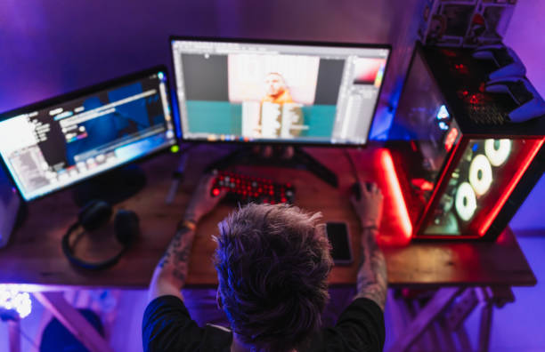 Professional Gamer Playing First-Person Shooter Online Video Game on His Powerful Personal Computer. Room and PC have Colorful Neon Led Lights. Young Man is Wearing a Cap. Cozy Evening at Home.