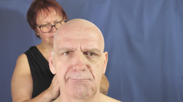Middle aged man has a sad face because his head is being shaved. Blue background