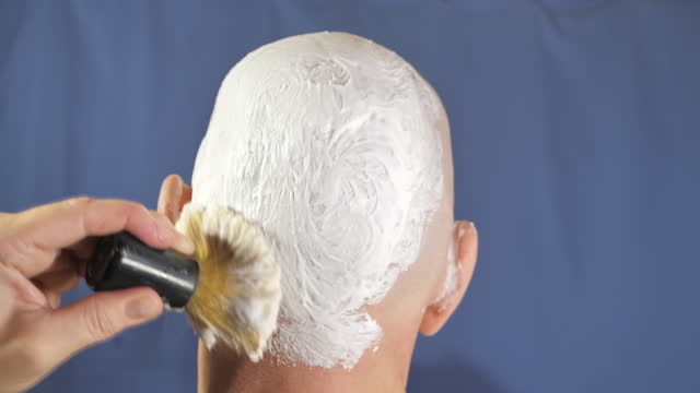 Lots of white shaving cream being brushed on the head