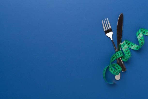 Knife and fork wrapped in tape measure on color background, top view