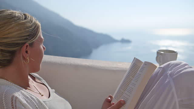 Woman reading a book on a villa balcony or terrace in Praiano Italy. The sea and the Amalfi coast can be seen