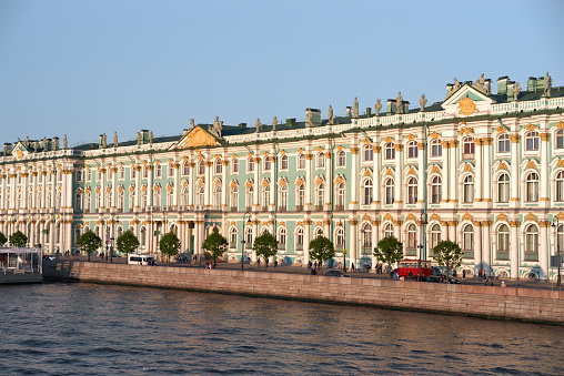 Sankt-Petersburg, Russia - June 10, 2023: Winter Palace in past, Hermitage Museum now in St. Petersburg, Russia. Neva river embankment. The Winter Palace was the official home of Russian monarchs until 1917. It now houses the Hermitage Museum and contains one of the world's greatest art collections. Evening yellow light, clear blue sky