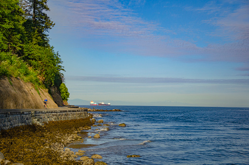 A cyclist riding across the seawall on a sunny day in Stanley Park, Vancouver, BC