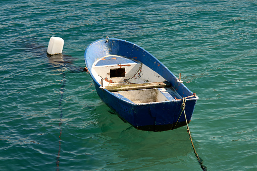 Blue auxiliary boat with a float that is a bottle and tied by a rope to the dock