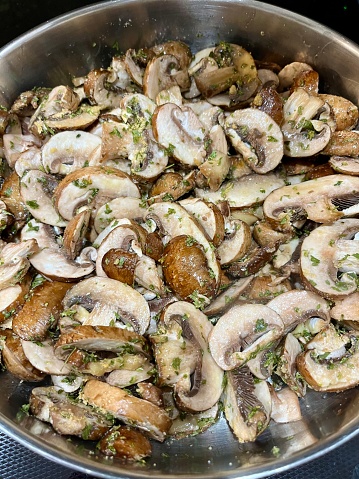The top down view of a pan with cut mushrooms, seasonings, and herbs.