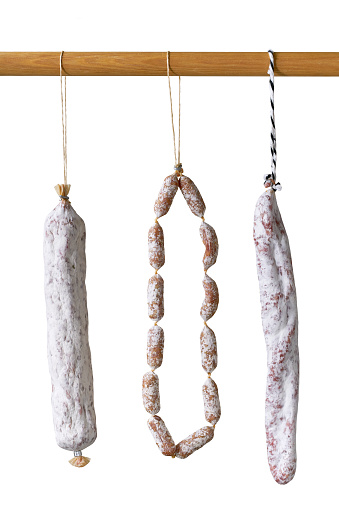 different types spicy pork fermented dry cured salami sausages hanging on the pole isolated on a white background.