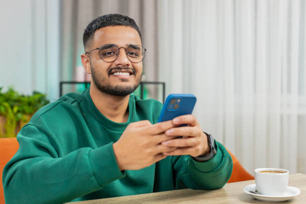istock Indian Arabian young man sitting at table use smartphone share messages on social media application 2046625397