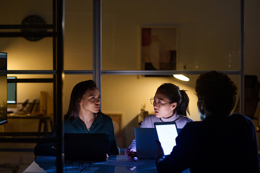 Ethnically diverse man and women working together in office late in evening discussing project