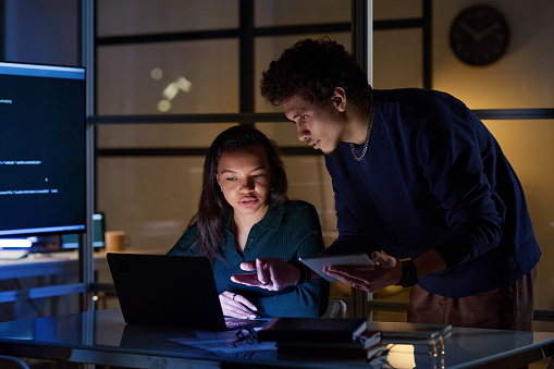 Ethnically diverse young male and female programmers working together on code in IT company office at night