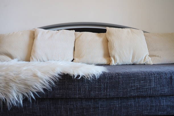 gray sofa with rough upholstery fabric boucle and white decorative fluted cushions. a long pile white faux fur rug or coverlet is thrown over the seat. living room interior - homewares cushion fake fur blanket ストックフォトと画像