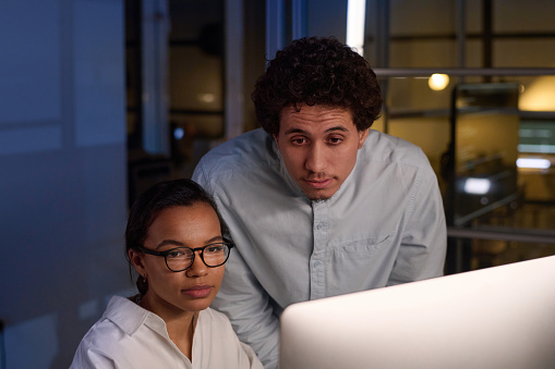 Biracial man and woman working on project at workplace in modern IT company office at night