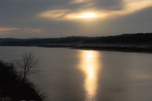 The reflection of the setting sun on the surface of Lake Travis mirrors the celestial spectacle above, transforming the water into a shimmering canvas of vibrant colors. The ripples on the lake catch and scatter the light, creating a dynamic interplay of shadows and highlights.