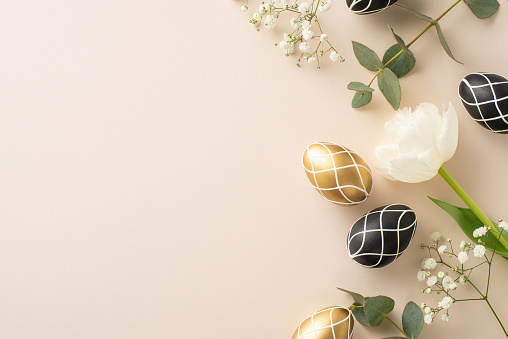 Opulent Easter theme: top view vertical photo of black and gold eggs, eucalyptus leaves, gypsophila clusters, tulip arrayed on a light beige base, with empty space for textual content