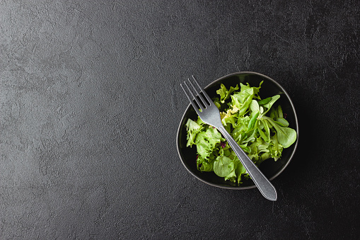 Green salad leaves in bowl on black table. Fresh and healthy food with copy space. Top view.