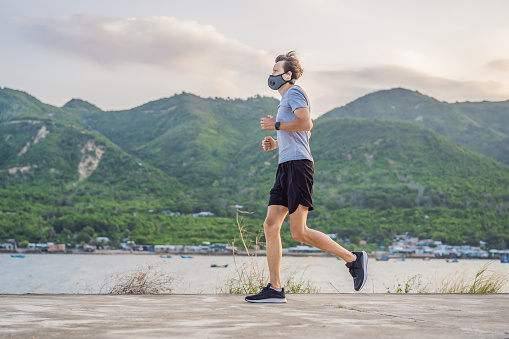 Runner wearing medical mask, Coronavirus pandemic Covid-19. Sport, Active life in quarantine surgical sterilizing face mask protection. Outdoor run on athletics track in Corona Outbreak.