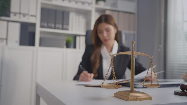 Asian lawyer woman work with hammer and scales of justice in courtroom. Attractive judge attorney looks at paper and document while sitting on table in office. Law and Legal business services concept.