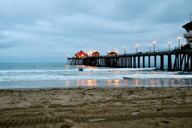 Huntington Beach Pier at dawn under a cloudy sky with lights reflecting in the water