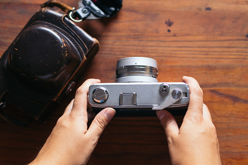 Close-up of an analog camera on a wooden table. An unrecognizable person is holding it.