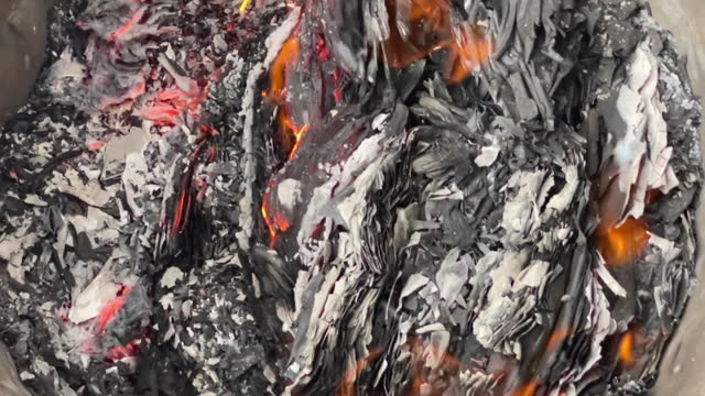 Slow motion shows embers and ashes smoldering in trash can