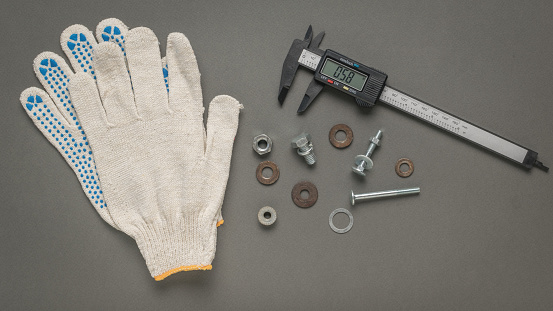 Gloves, a fastening tool and an electronic vernier caliper on a gray background. A tool for accurate measurement of dimensions.