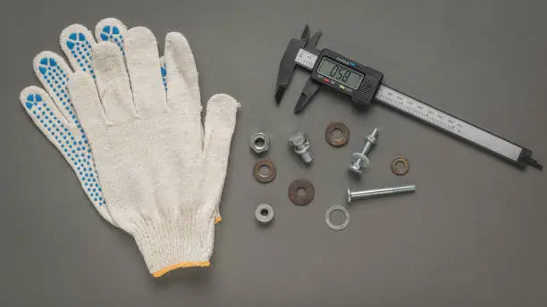 Photo of Gloves, a fastening tool and an electronic vernier caliper on a gray background.