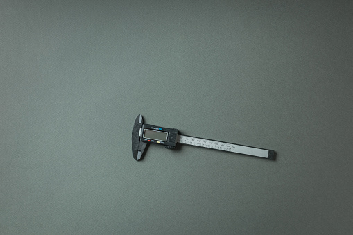 An electronic vernier caliper with a display on a gray background. A tool for accurate measurement of dimensions.