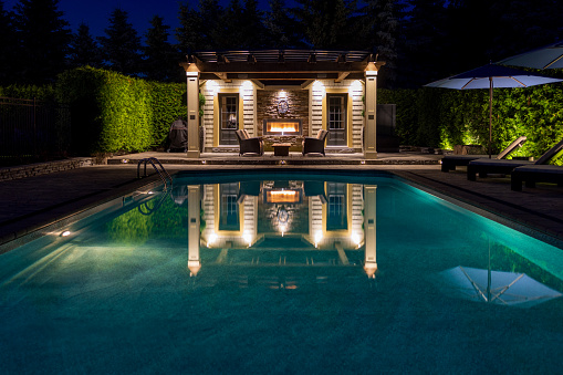 Beautiful residential pool and cabana with pergola, fireplace and sitting area lit at night