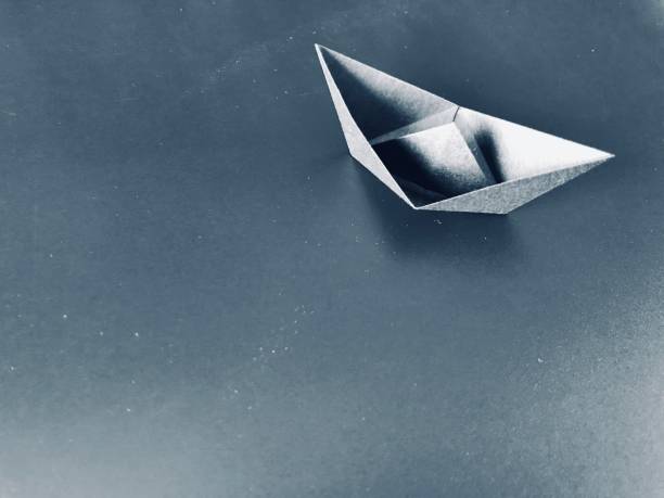 origami gray paper boat on the clear gray table with copy space at the left side of the frame