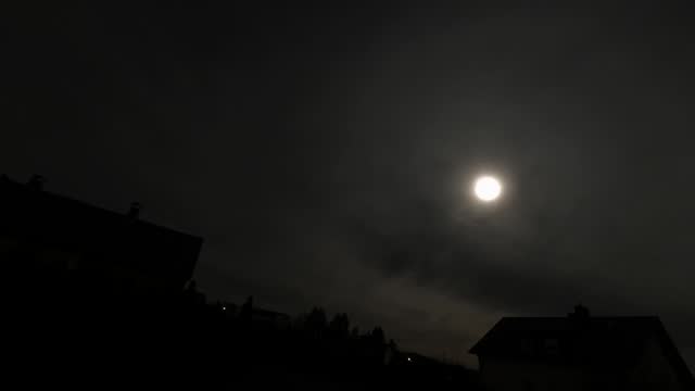 Low angle timelapse shot of the clouds moving around the glowing full moon over the city buildings