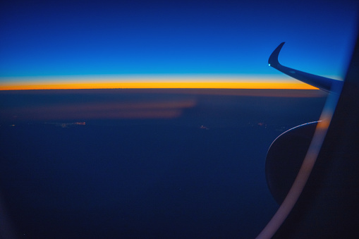 Looking at the sunrise through an airplane window. The horizon can be seen with gold and blue colours