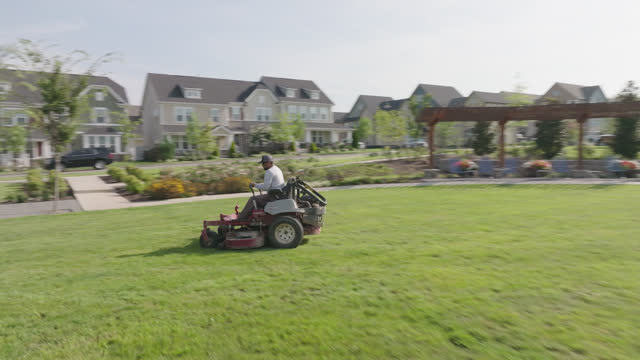 Follow Shot of a Man Using a Riding Lawnmower to Cut Grass in Straight Lines