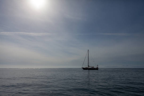 Small Sailboat Sailing on a Sparkling Sea Horizon Against a Vast Blue Sky