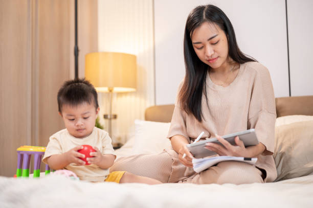 istock A beautiful Asian mom is working on her digital tablet while her bay boy is playing toys in bed. 2047085378