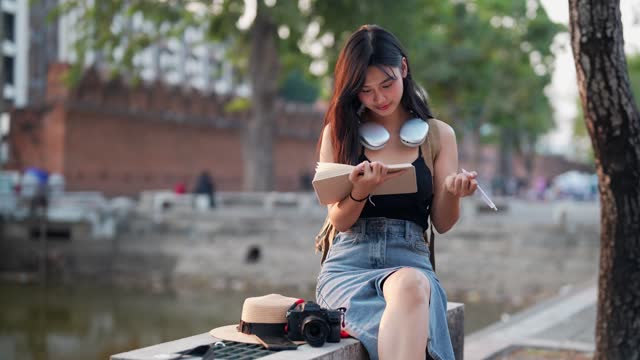 Asian female traveler using a diary and relaxing at a tourist spot in a northern province of Thailand